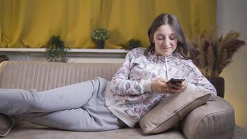 joven mujer acostado en el sofá a noche mensajes de texto en el teléfono. contento y en bueno espíritu. video