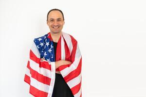 Happy relaxed satisfied handsome middle aged man standing wrapped in USA flag, celebrating national holiday, wearing urban style hoodie. Indoor studio shot isolated on white background. photo
