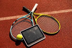 High angle view of tennis racket and ball by digital tablet on maroon background photo