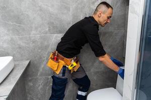 Professional plumber in uniform fixing toilet tank indoors photo