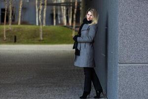 Beautiful young stylish blonde woman wearing long coat walking through the city streets. Trendy casual outfit. Street fashion. photo