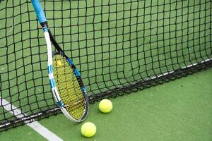 Tennis racket and tennis ball besides the net on outdoor tennis court. photo