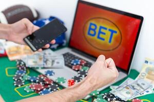 Close up cropped shot of male hands making bets using gambling mobile application on his phone. Man watching football match online broadcast on his laptop waiting for winning results. Bet wins. photo