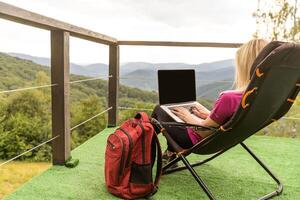 A woman in a sports warm suit works on a laptop outdoors in a mountainous area. photo
