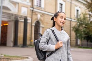 linda joven niña con un mochila Bóveda a colegio en frío otoño Mañana. foto