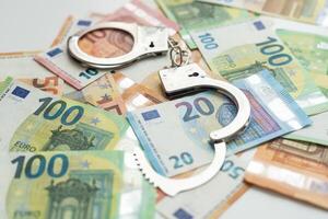 Pair of metal police handcuffs on Euros banknotes money cash background. Corruption, dirty money, gambling or financial crime ideas concept. photo