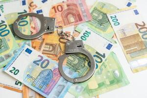 Pair of metal police handcuffs on Euros banknotes money cash background. Corruption, dirty money, gambling or financial crime ideas concept. photo