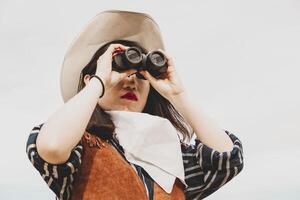 cute chinese cowgirl while looking at the horizon with binoculars photo