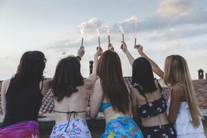 Group of happy female friends holding sparklers at rooftop party photo