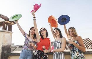 grupo de hembra amigos teniendo divertido mientras Bebiendo rojo vino en el techos foto