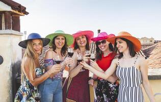 group of female friends wearing hats toasting red wine photo