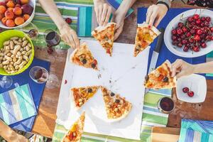 hands of girlfriends share slices of pizza from a table photo