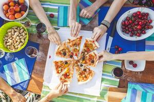 hands of girlfriends share slices of pizza from a table photo