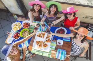 group of female friends wearing colorful hats toasting with red wine to celebrate on a terrace photo