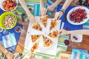 hands of girlfriends share slices of pizza from a table photo