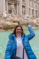 contento medio Envejecido hembra turista en vacaciones lanzamiento un moneda en el agua de famoso trevi fuente en Roma foto