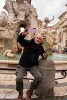 contento medio Envejecido hombre en vacaciones tomando un selfie en frente de el fuente en plaza navona en Roma foto