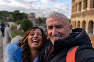 contento medio Envejecido Pareja en vacaciones tomando un selfie en frente de Coliseo anfiteatro en Roma foto