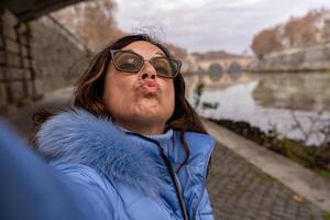 happy middle aged woman on vacation taking a selfie on the banks of the Tiber river in rome photo