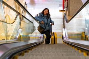 beautiful middle aged woman using escalator leaving for vacation with a yellow trolley photo
