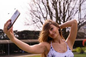 joven encantador rubia deportivo mujer en ropa de deporte posando tomando un selfie al aire libre foto