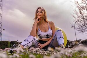 young beautiful blonde woman in tight sportswear doing light gymnastic exercises outdoors in a field of daisies photo