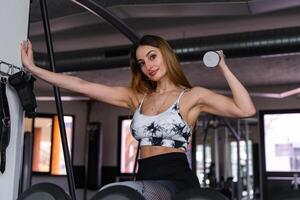 young charming blonde woman in sportswear lifting dumbbells in a gym photo