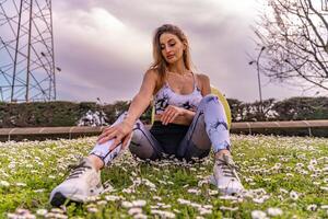 young beautiful blonde woman in tight sportswear doing light gymnastic exercises outdoors in a field of daisies photo