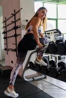 young charming blonde woman in sportswear lifting dumbbells in a gym photo