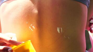 femme écran solaire épaule. proche en haut sur main de content souriant Jeune femme est appliquant crème solaire ou Soleil bronzage lotion sur une dos. prendre se soucier de peau sur une bord de mer plage pendant vacances vacances. video