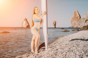 mujer mar sorber. cerca arriba retrato de contento joven caucásico mujer con largo pelo mirando a cámara y sonriente. linda mujer retrato en un azul bikini posando en cenar tablero en el mar foto