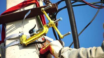 Skilled electrician in helmet fixes wires standing on ladder near high pole against blue sky on summer day backside view. Electrical service and mounting on the pole. Slow motion video