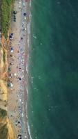 antenne visie van zanderig strand, zwemmen mensen in zee baai met transparant blauw water Bij zonsondergang in zomer. gelukkig mensen menigte ontspannende Aan strand. vakantie recreatie oceaan natuur concept. verticaal video