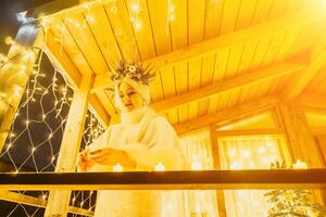 Happy smiling woman in a white dress lighting candle in front of a Christmas tree. photo