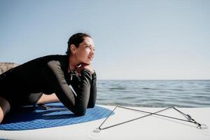 mujer cenar yoga. contento deportivo mujer practicando yoga pilates en paleta cenar tabla de surf. hembra extensión haciendo rutina de ejercicio en mar agua. moderno individual hembra hipster al aire libre verano deporte actividad. foto