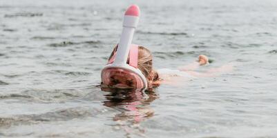 Young happy woman in white bikini and wearing pink mask gets ready for sea snorkeling. Positive smiling woman relaxing and enjoying water activities with family summer travel holidays vacation on sea. photo