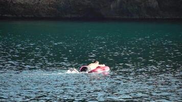 estate vacanza uomo galleggia su un gonfiabile ciambella materasso, un' acqua giocattolo nuotare squillo. positivo contento uomo rilassante e godendo famiglia estate viaggio vacanze vacanza su il mare. lento movimento video