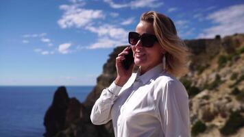 företag kvinna talande förbi telefon på de hav. digital nomad, Söt lady skriver på dator förbi de hav på solnedgång, gör en företag transaktion uppkopplad från en distans. frilans, avlägsen arbete på semester video