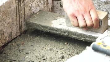 Construction, Worker Hands smooth wet cement in wooden frame at a construction site during daytime to ensure an even surface video