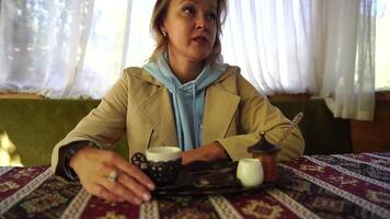 Woman pouring Turkish coffee from cezve into cup. Closeup slow motion shot of female hand with cup on square plate, on table in cafe outdoor. Traditional hot unfiltered coffee served in restaurant video