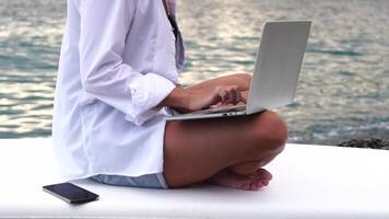 digital nomad, företag kvinna arbetssätt på bärbar dator förbi de hav. Söt lady skriver på dator förbi de hav på solnedgång, gör en företag transaktion uppkopplad från en distans. frilans, avlägsen arbete på semester video