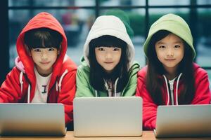 AI generated Three 10 yo Asian children in hoodies sitting in front of open laptops, looking at camera. Childhood, technology, education, online learning concept. smm, blogs, internet articles photo