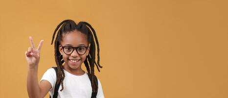 AI generated black little girl 10 years old, smile, looking at camera, glasses, pupil points with his finger to the side on yellow background, hand pointing empty place, Advertising banner photo