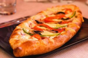 Peinirli greek open faced pizza with cheese, mushrooms and pepper served on the black plate on white background in greek tavern. Mediterranean cuisine. Selective soft focus photo