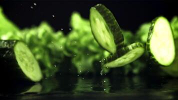 Pieces of fresh cucumber fall on the table with splashes of water. On a black background. Filmed is slow motion 1000 fps. High quality FullHD footage video