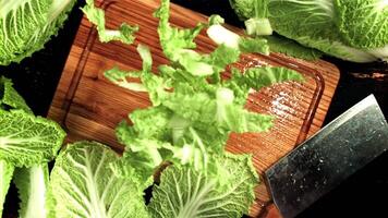 Sliced Beijing cabbage falls on a wooden cutting board. On a black background. Top view. Filmed is slow motion 1000 fps. video