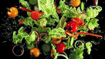 een levendig salade van sla, tomaten, wortels, en andere groenten sierlijk valt in de water tegen een zwart achtergrond in een boeiend en verfrissend zichtbaar Scherm hoog kwaliteit video