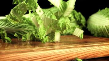 Sliced Beijing cabbage falls on a cutting board. On a black background. Filmed is slow motion 1000 frames per second.High quality FullHD footage video