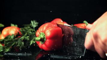 A man's hand cuts a sweet pepper into two halves with a knife. On a black background. Filmed is slow motion 1000 frames per second. video