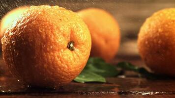 Drops of water with splashes fall on fresh oranges. On a wooden background.Filmed is slow motion 1000 frames per second. High quality FullHD footage video